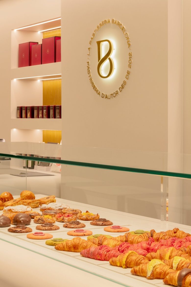Витрина с выпечкой и фирменным логотипом на стене La Pastisseria Barcelona
